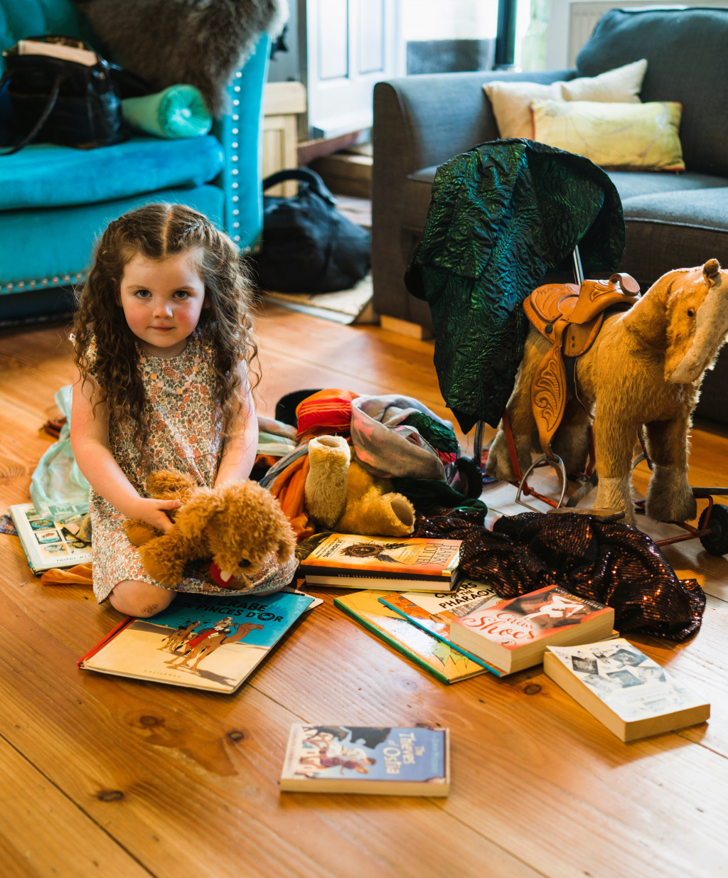 Little girl with books and toys on wooden floor