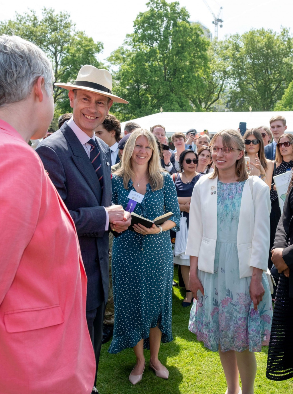 Two ladies in garden party dresses talk to Duke of Edinburgh