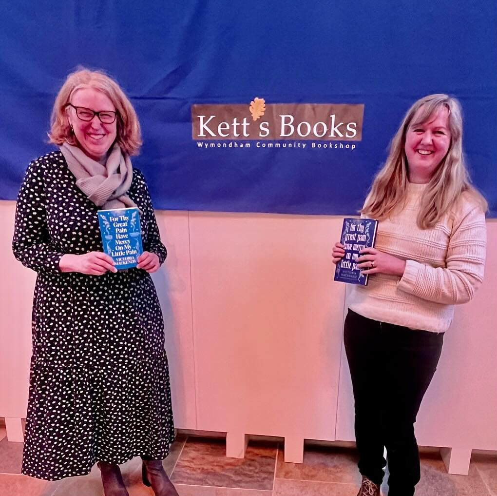 Two women holding books standing in front of kett's books banner