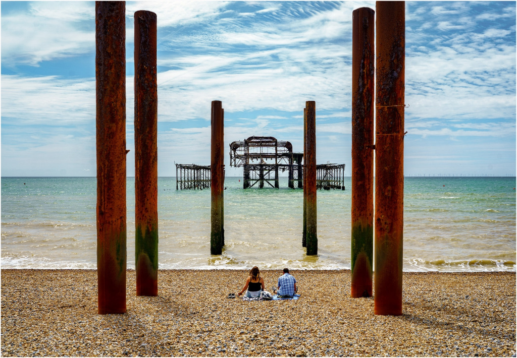Couple on beach with blue partly cloudy sky framed by red columns